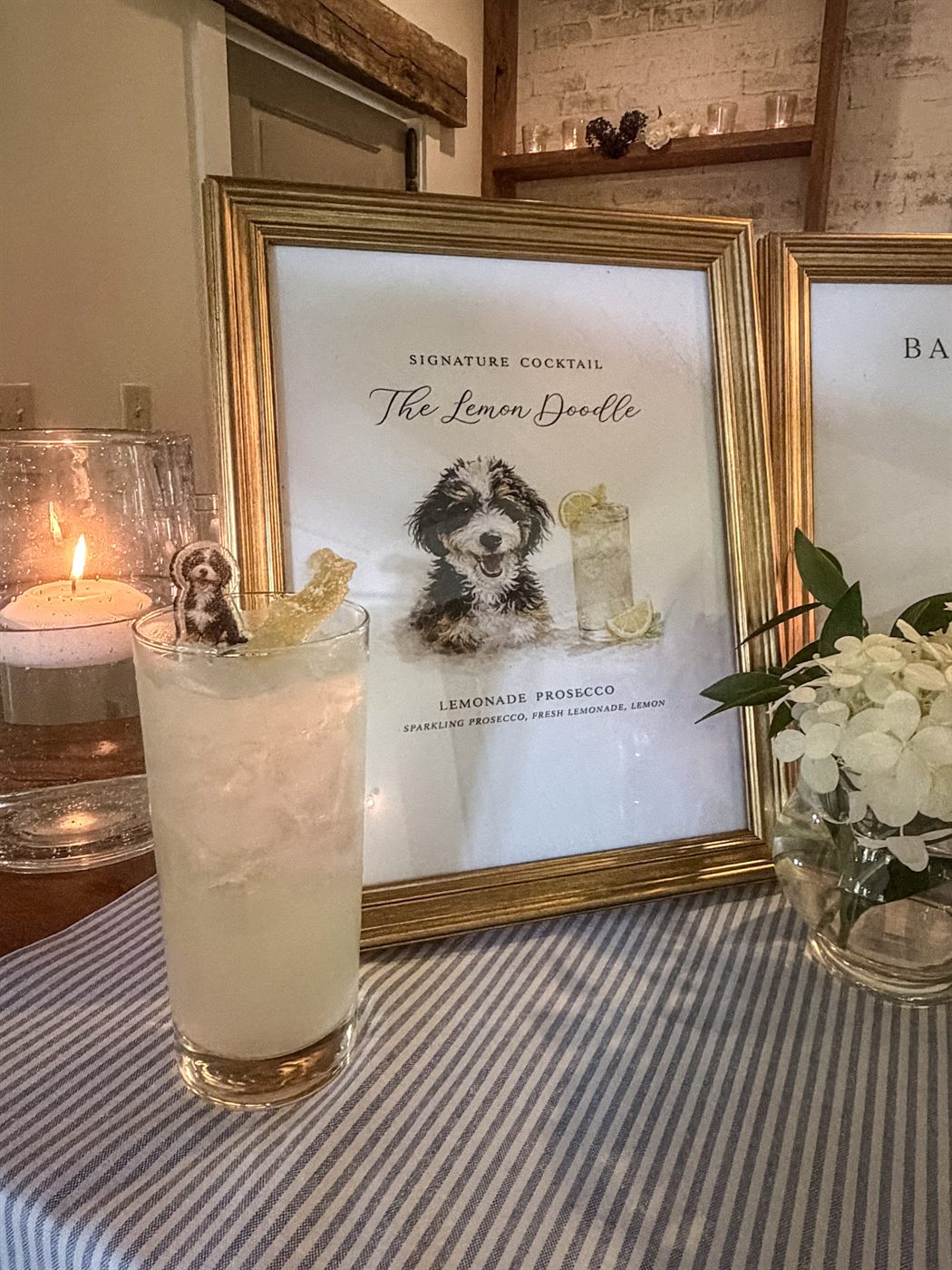 The Lemon Doodle signature cocktail beside its framed menu card, garnished with candied lemon and a cutout of the couple's dog