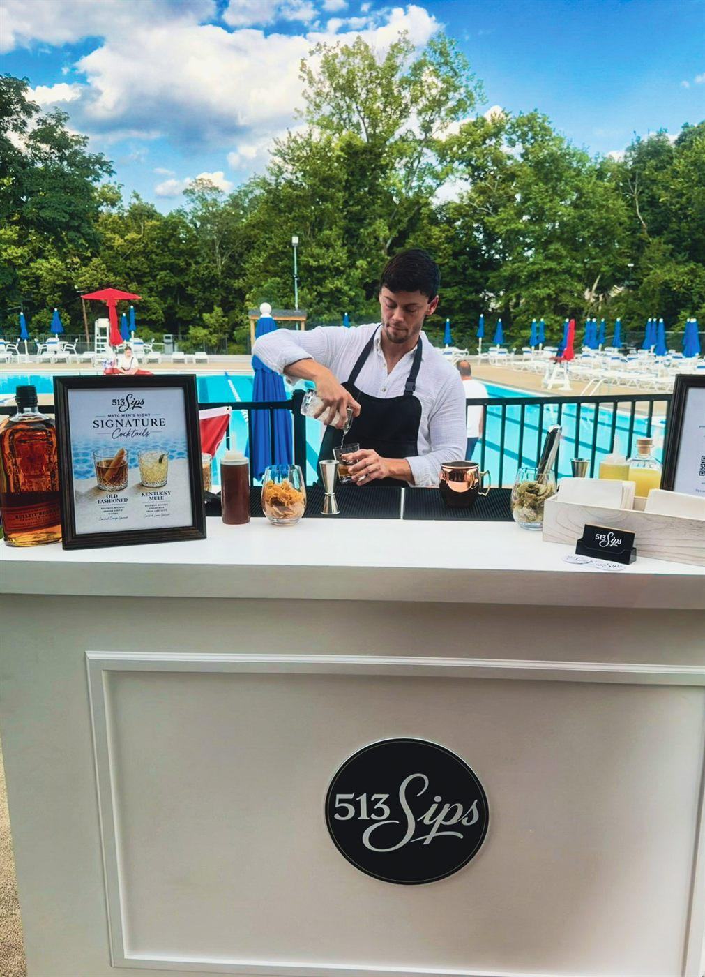 The 513Sips mobile bar set up on the pool deck at Montgomery Swim and Tennis Club, with a bartender pouring a cocktail